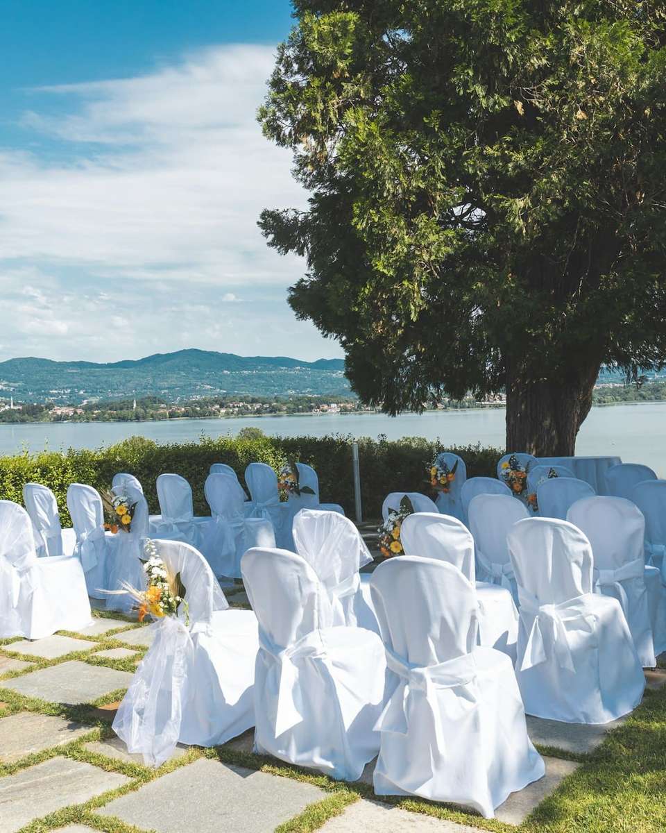 Sillas con funda blanca preparadas para una ceremonia al aire libre junto a un lago