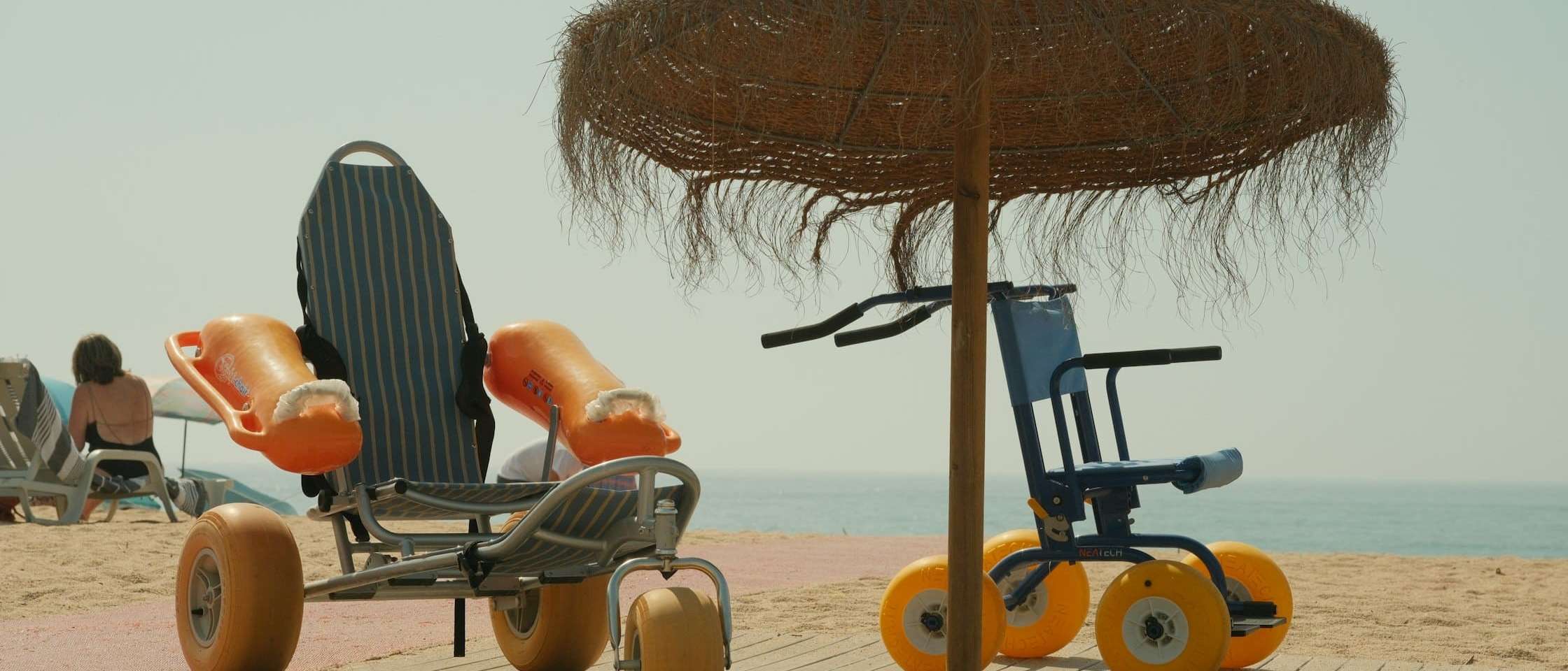 Sillas anfibias para personas con movilidad reducida bajo una sombrilla de brezo en la playa