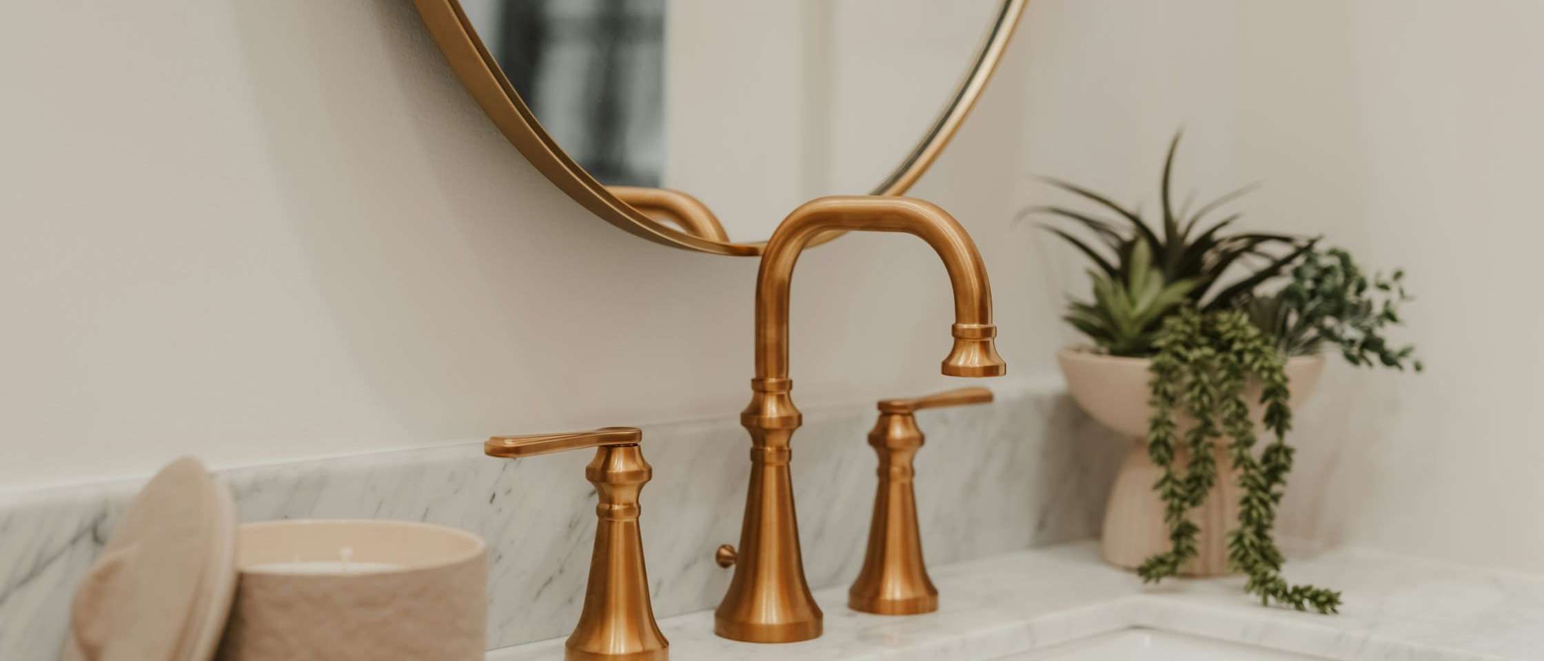 Lavabo de mármol blanco con grifería de cobre y espejo redondo con marco dorado