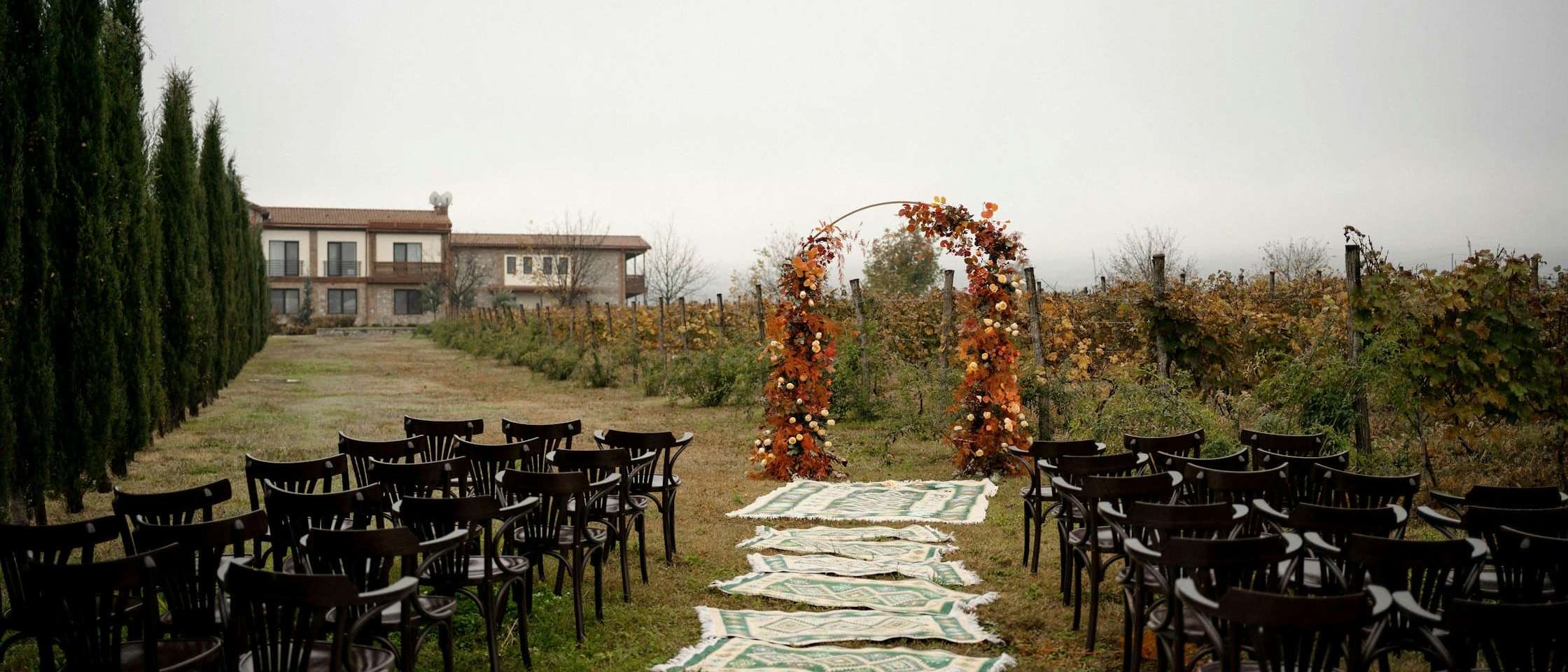 Ceremonia de boda al aire libre preparada entre viñedos, con pasillo de alfombras y arco de flores