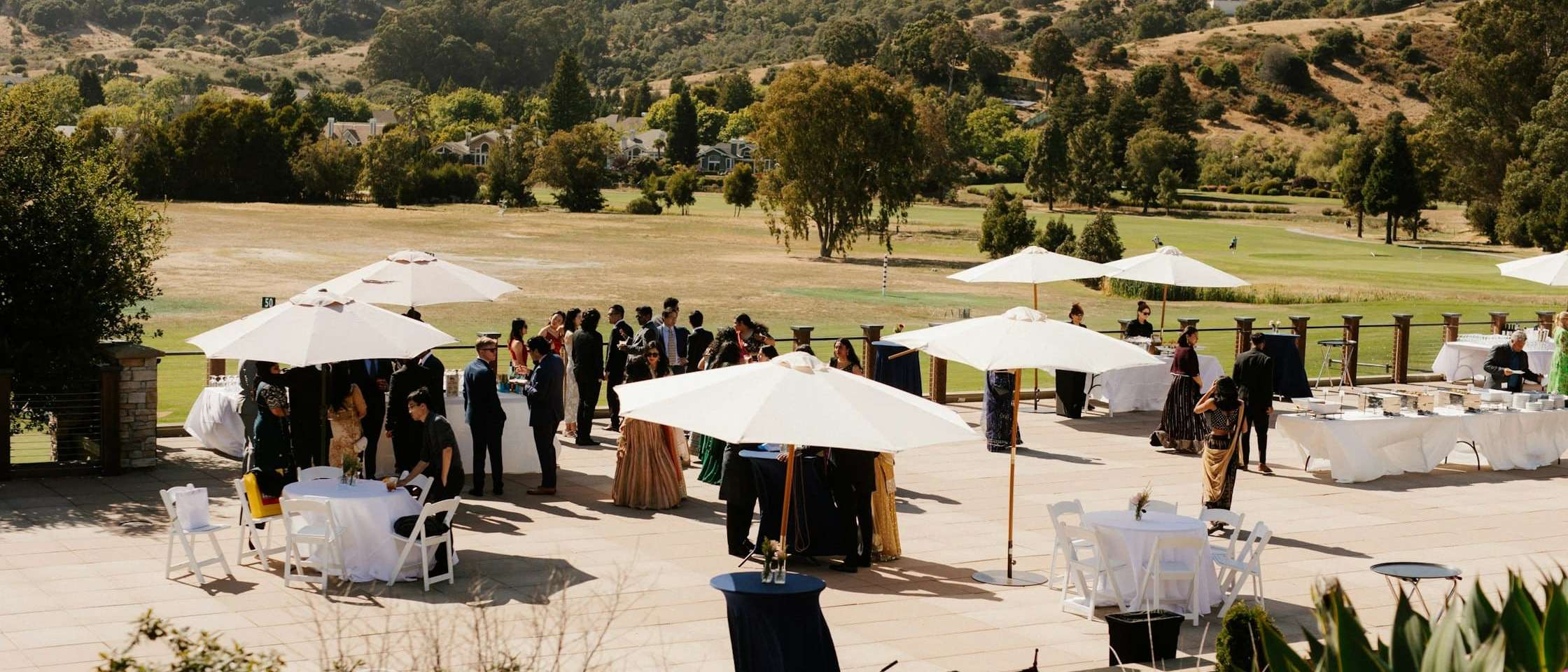 Cóctel de empresa al aire libre con sombrillas blancas y mesas altas en una terraza con vistas al campo