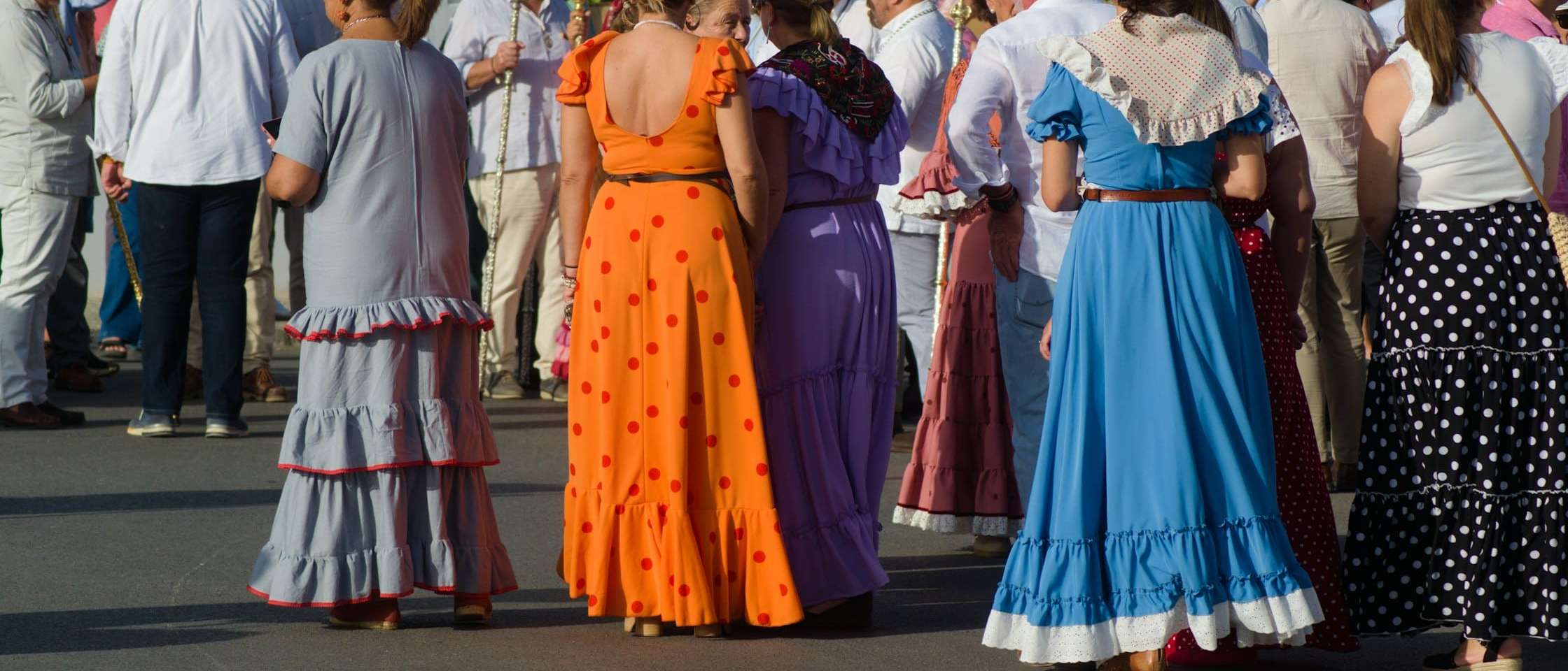 Mujeres con trajes de flamenca, de espaldas, en una calle durante una romería