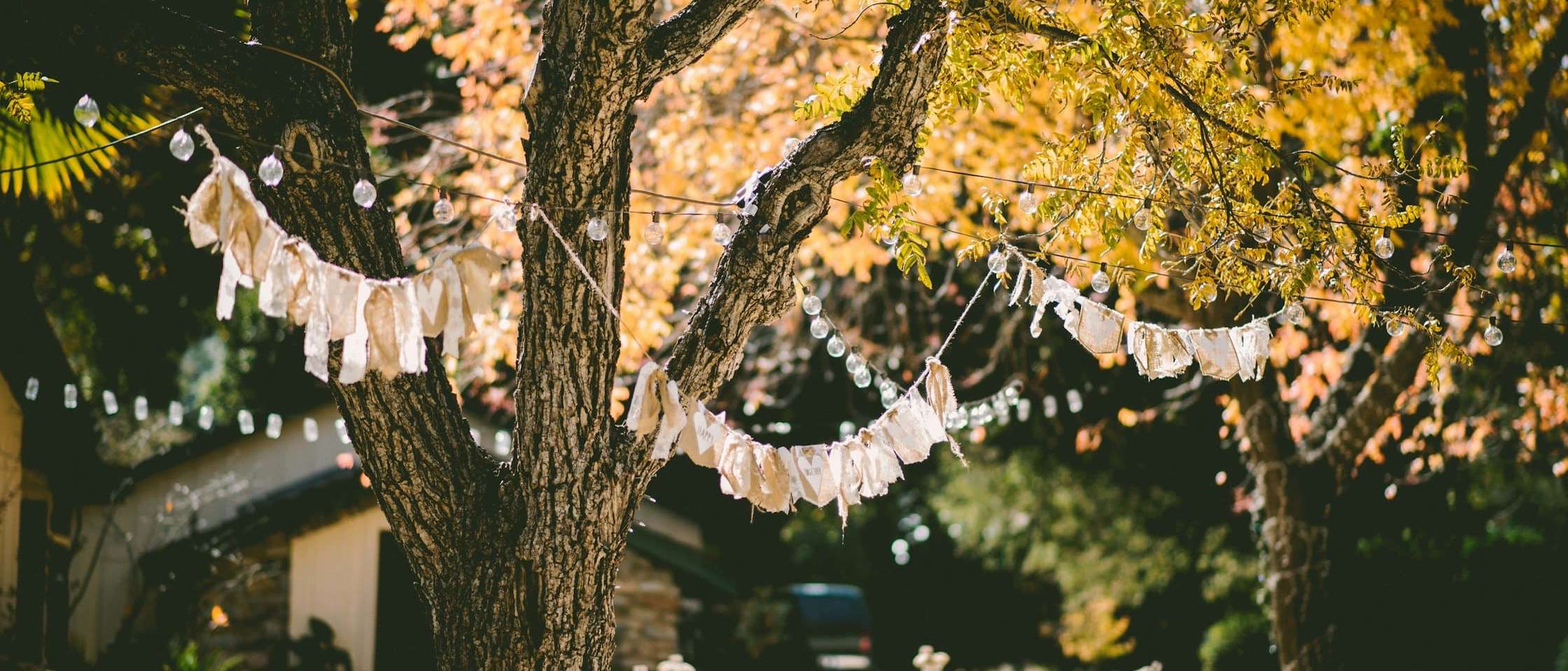 Jardín preparado para una fiesta con banderines, guirnaldas de luces y mesas con mantel blanco