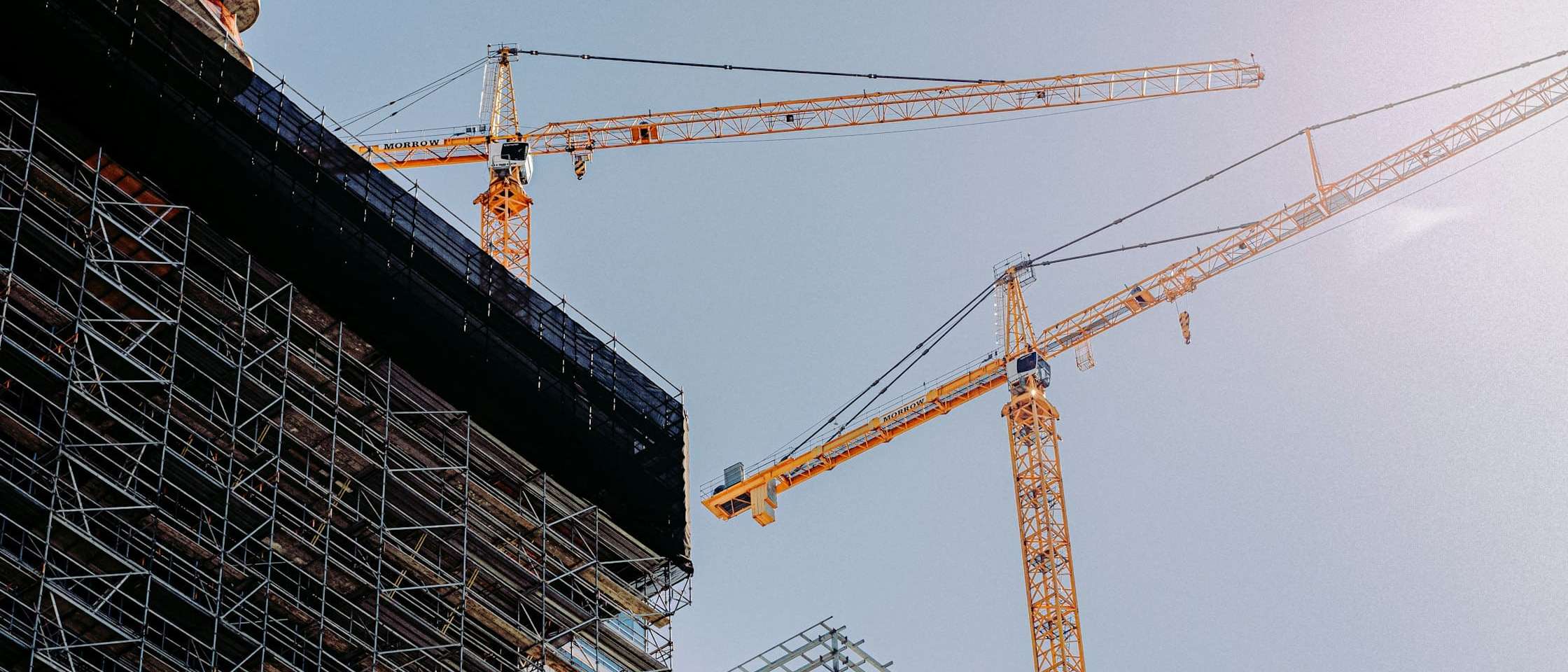 Edificio en construcción con andamios y dos grúas torre